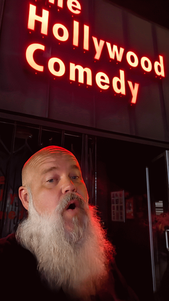Ken Cox outside The Hollywood Comedy beneath its red neon sign.